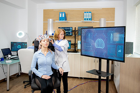医生跟踪脑波在大型监视器上扫描耳机传送的数据的追踪博士屏幕科学家女性网络头脑设施活动技术药品椅子图片
