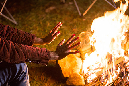 年轻人在营火上暖和他的双手帐篷火焰旅游火树林星星时间森林营地团体乐趣图片