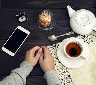 女人的手躺在木制桌子上 旁边是一杯茶和一杯S图片