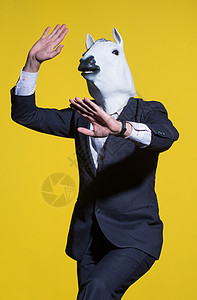 黄色背景上戴着马面具的男人狂欢摄影商务海报西装多样性工作戏服男性动物图片