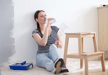 青年妇女坐在地板上 水瓶放在油漆刷子旁边图片