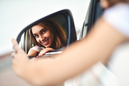 可爱笑笑女孩的肖像 坐在车里 看着汽车镜子图片