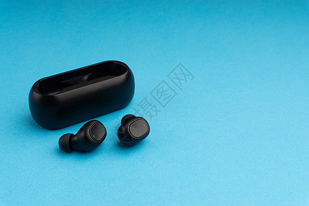 蓝色背景上的无线耳塞或耳机黑色蓝牙工具波浪耳朵收音机助听器立体声充电音乐图片