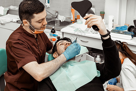 一位年轻的男牙医在治疗病人 牙科 外科的医疗操作 牙医的专业制服和设备 医疗保健装备医生工作场所 牙科口服卫生员程序口腔科卫生牙图片