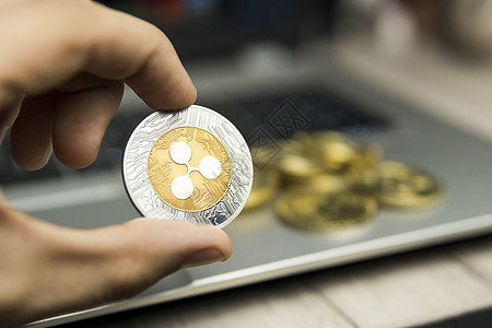 男性商务人士手持Ripple硬币 背景是笔记本电脑键盘和一堆金质硬币 虚拟货币和金融增长概念 Ripple贸易采矿时间商业市场密图片