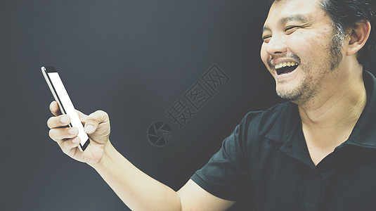 亚洲男人在深色风格中使用智能手机微笑电话快乐乐趣胡须黑色衬衫成人头发马球旅行图片