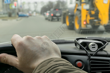 在附近一辆过路拖拉机的背景下骑在城市公路上的汽车方向盘上看到司机手的动向 Name图片