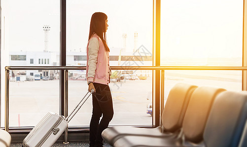 旅行生活方式的概念 出发前在登机口航站楼等候的旅行女游客带着行李在机场窗口看着日出的飞机进行早班飞行图片