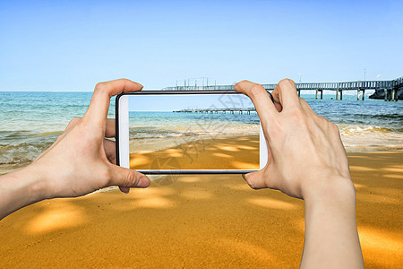 女孩用移动智能手机拍照 在波在沙滩上b图片