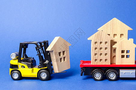 一辆黄色的叉车将一个木制的房子模型装载到卡车上 运输和货物运输 搬家公司的概念 建造新房屋和物品 行业 移动整个建筑物销售送货财图片