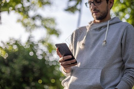 聪明帅哥在公园的智能手机上发短信 背面细胞男性电话互联网技术工具社会背景图片