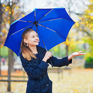 带着伞女孩秋天或春季下雨日 在卢森堡巴黎花园的卢森堡花园中带蓝伞的年轻女子淋浴女士树叶叶子预报花园天气成人城市沉淀背景