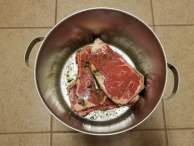 牛肉牛排 在瓷砖地板的金属锅里加调料和液体图片