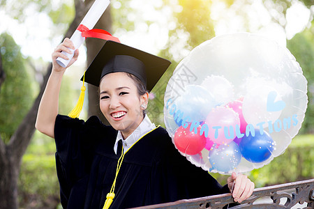 穿着学术服和学校服装的年轻快乐女毕业生肖像帽子长袍学士成功证书气球文凭幸福微笑成人图片