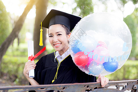 穿着学术服和学校服装的年轻快乐女毕业生肖像仪式大学学习微笑文凭教育长袍气球帽子研究生图片