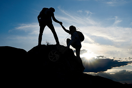 旅行者在日落山上远足 男子帮助妇女攀登顶峰 家庭旅行和冒险危险岩石友谊女士风险救援夫妻朋友运动蓝色图片