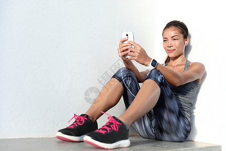 使用电话应用程序和智能观察健身跟踪器听音乐的女运动员图片