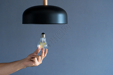 特写 手会改变一个灯泡 在时尚的阁楼灯 螺旋丝灯 现代室内装饰家务技术电气天花板安装家庭服务经济金子玻璃图片