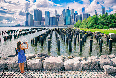 曼哈顿市天线水边生活方式 人们从布鲁克林桥公园1码头盐沼中走着享受市区风景的人 纽约旅游女游客用智能手机拍移动照片图片