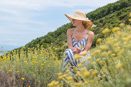穿着条纹夏装和草帽的年轻女子坐在盛开的野花中 一边放松一边享受克罗地亚亚得里亚海沿岸自然的美丽自然图片