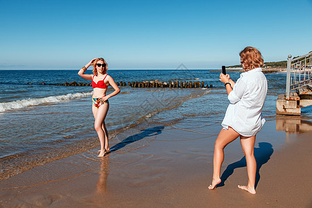 两个穿泳装的女生 互相用聪明人拍相照快乐图画相机朋友街道女性冒充金发女郎衬衫女士图片