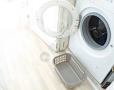 一台开着门的洗衣机和一个用来装刚洗好的衣服的小塑料篮图片