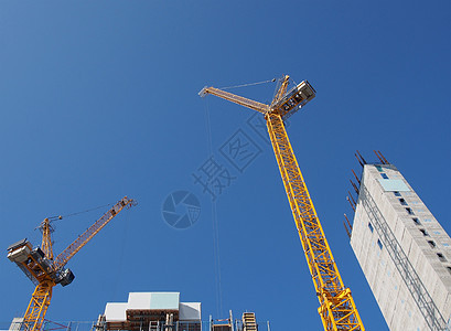 两台高大的黄色塔式起重机在一个大型住宅建筑工地上工作 在蓝天上有一座大型混凝土塔图片