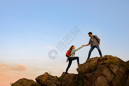 旅行者在日落山上远足 男子帮助妇女攀登顶峰 家庭旅行和冒险伴侣运动日落夫妻男人高度救援日出远足者危险图片