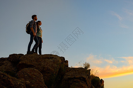青年旅游者在夏季日落时站在岩石顶端 家庭旅行和冒险概念组织阳光女士登山者远足者团队夫妻高度风险伴侣男人图片