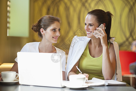 在咖啡馆使用手机与朋友坐在一起的年轻女子图片