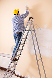 年青的承包商用砂纸铺沙墙承包商职业工具工人房子梯子磨料画家建设者装潢师图片