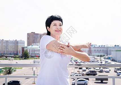 微笑的老年妇女在城市背景上做户外伸展活动女士成人福利身体运动装力量运动闲暇训练运动员背景图片