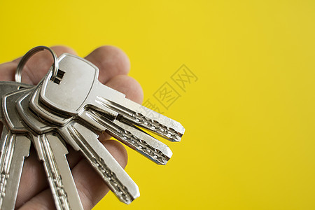 男士手拿着一组黄色背景的钥匙 房地产经纪人为客户提供公寓钥匙 专注于按键 房地产经纪人手中的一串钥匙房东建筑成功代理人销售女士家图片