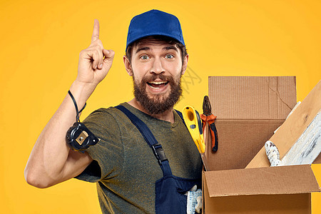 男人在工作形式中 一个装有装填工具的盒子中的黄色背景货物运输邮件人士服务纸板商务包装装载机重量背景图片