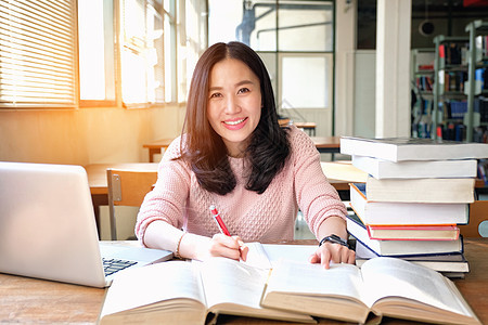 年轻女性在学习libra时注意到并使用笔记本电脑知识学校阅读女孩学生大学教育女士书架微笑图片