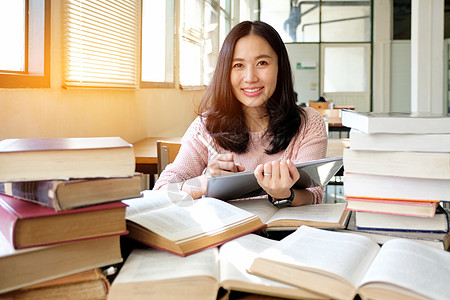 在图书馆使用平板板的年轻妇女笔记本电脑阅读耳机微笑青少年药片大学书架校园图片