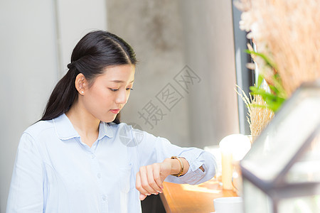 女士手表美丽的亚洲年轻女子看着等待朋友或朋友的手表咖啡店员工工作小时餐厅女孩店铺女性咖啡检查背景