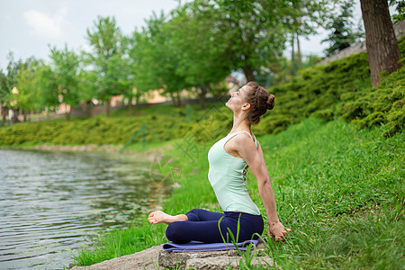 一名年轻运动女运动员在河边绿草坪上做瑜伽 瑜伽屁股的姿势 与自然的思考和团结瑜珈力量锻炼灵活性训练女孩健身房冥想沉思海滩图片