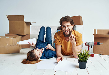一个女人男人在花盆里躺在地板上 在沙发附近的一间明亮的房间里幸福白色纸板成人家庭盒子搬迁女性抵押公寓图片