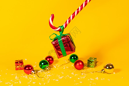 糖果手杖棒棒糖拿着一个礼盒 里面有黄色背景的圣诞礼物 圣诞糖果和新年装饰季节展示丝带风格盒子甜点礼物装饰品送货传统图片