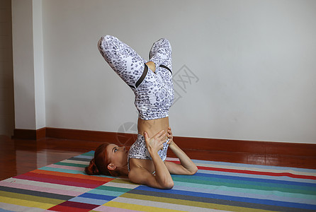 做追风少年妇女在家里做瑜伽运动身体成人训练灵活性女孩体操运动装姿势地面背景