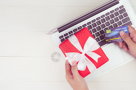 手持信用卡和网上购物的人的手 用于在木制背景上赠送带笔记本电脑的礼品盒 在圣诞节或假期在办公桌上庆祝 顶视图 平躺庆典键盘礼物桌图片