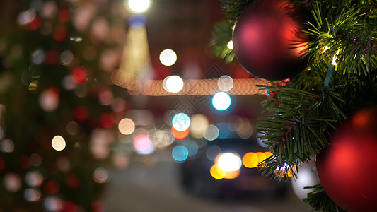 在模糊的闪闪发光的仙女背景上 用明亮的红球装饰的户外圣诞树的特写镜头 散焦花环灯散景效果 散焦的夜城街道 道路上有汽车夜生活宏观图片