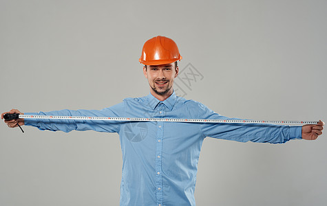 男性建筑商手手上有测量胶带 在灰色背景上工人头盔建筑师修理工商业建设者工作承包商工作室衬衫图片