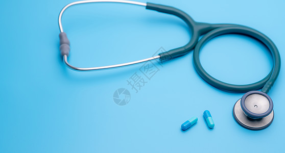 他汀类药物蓝色胶囊药丸和蓝色背景上的绿色听诊器 健康检查 用于心跳测试的心脏病学医生设备 医疗保健和医疗概念 用于诊断的诊断医疗工具抗菌剂背景