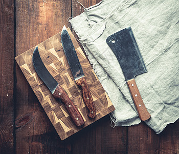 由棕色木板制成的桌子上的金属厨房刀和木板木头食物屠夫用具刀具餐厅工具烹饪餐巾团体图片