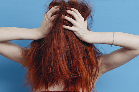 红头发女人用双手触摸头部 手感性情 头发被压断的蓝色背景图片