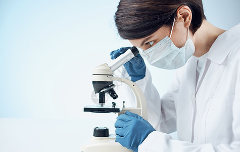 身穿医疗长袍和手套的女医生 在室内桌子上通过显微镜检查制药外套专注女性教育女士技术员微生物学工人测试图片