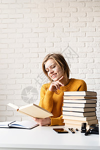 穿着黄色毛衣的年轻微笑女人 在读书和笑白色笔记本微笑教育办公室学生快乐学习技术闲暇图片