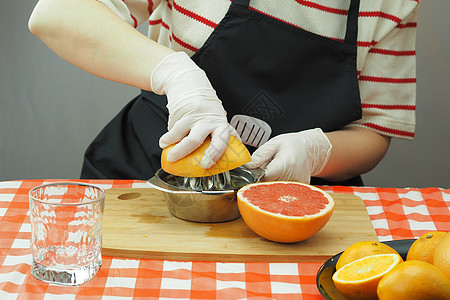 一位年轻女子用手工果汁机做的橙子和葡萄油做新鲜的榨汁服务员手套维生素厨房免疫婴儿柚子食品水果女士图片